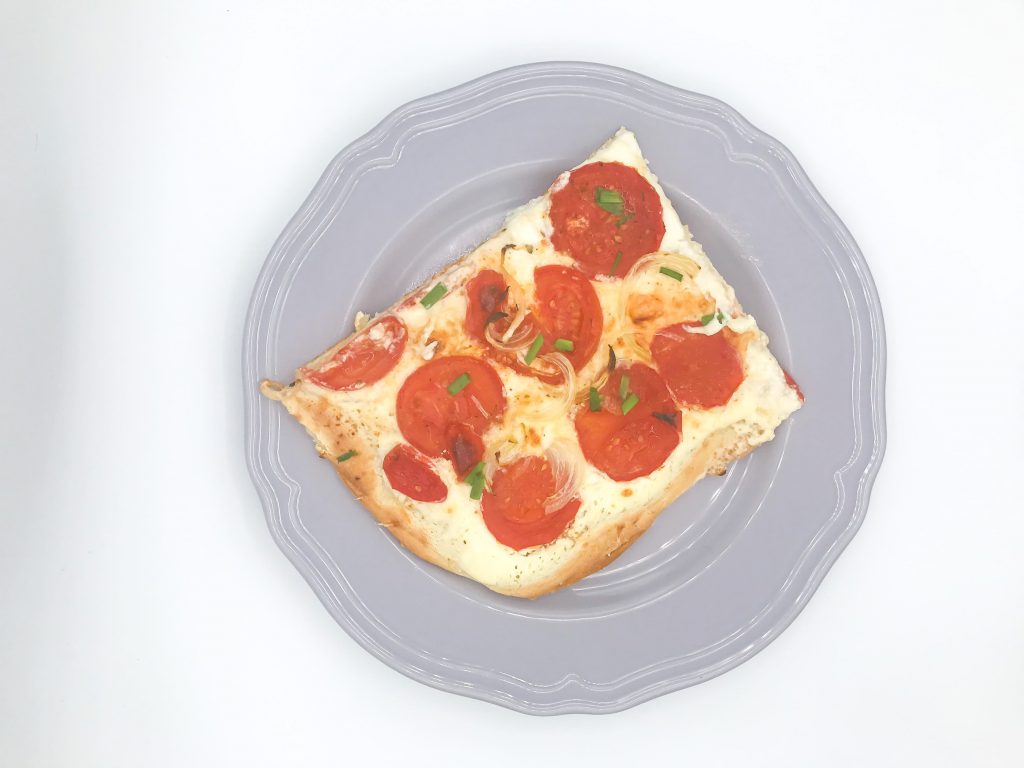 Ein Teller, darauf ein Stück Tomatenpizza, von oben fotografiert.