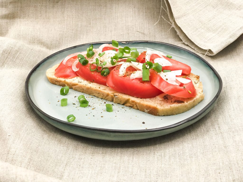Auf einem Teller: Eine Scheibe Bauernbrot, Tomatenscheiben, Zwiebeln und Frühlingszwiebeln.
